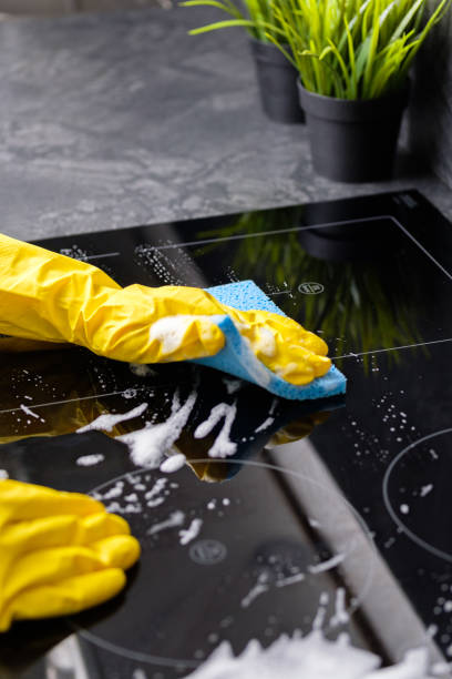 The girl washes the stove with a blue sponge in yellow gloves